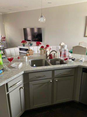 Modern kitchen with granite island, sink, and breakfast bar, opening to a bright living room with wall-mounted TV.