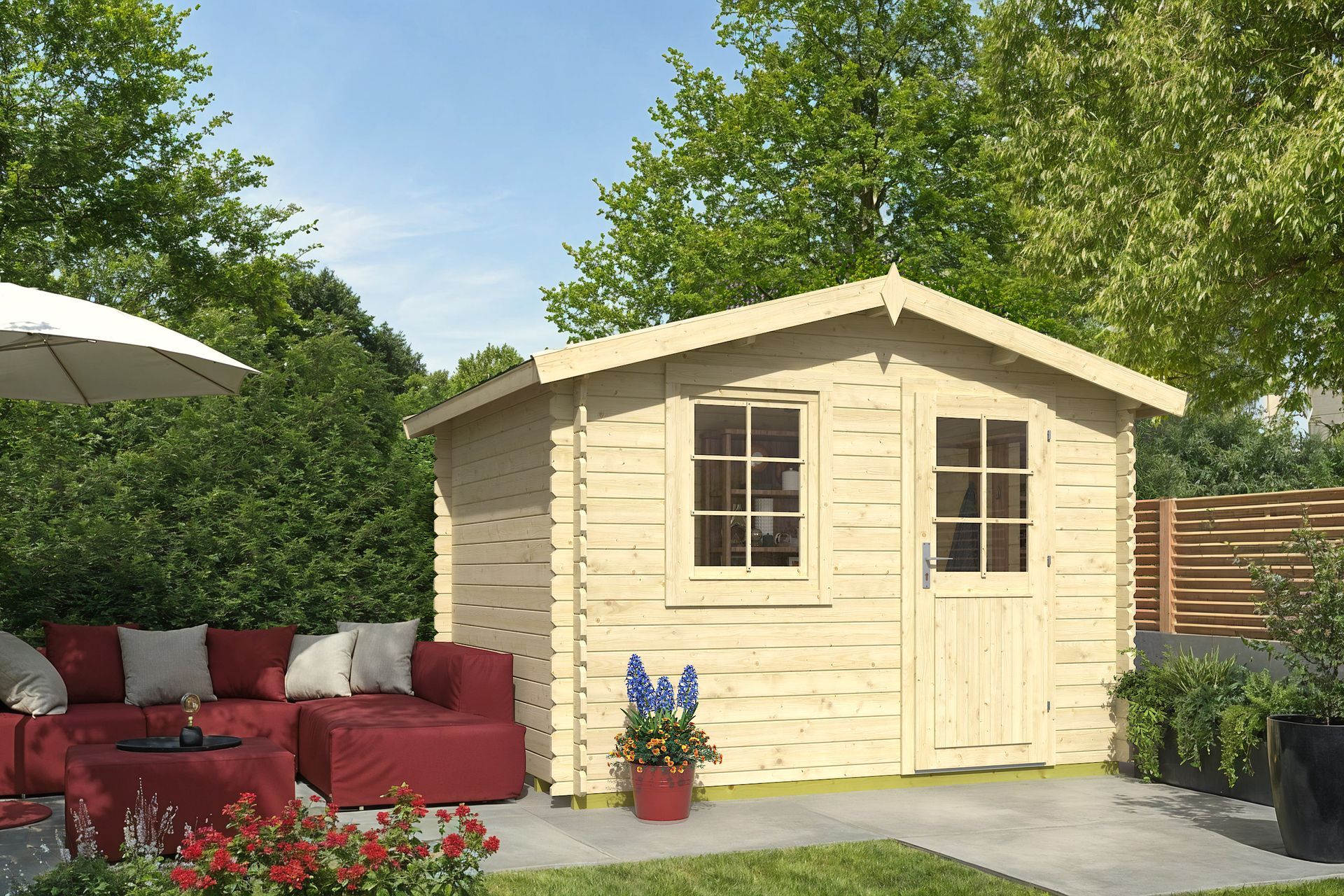 Beige garden shed in a sunny backyard beside red patio seating and greenery.