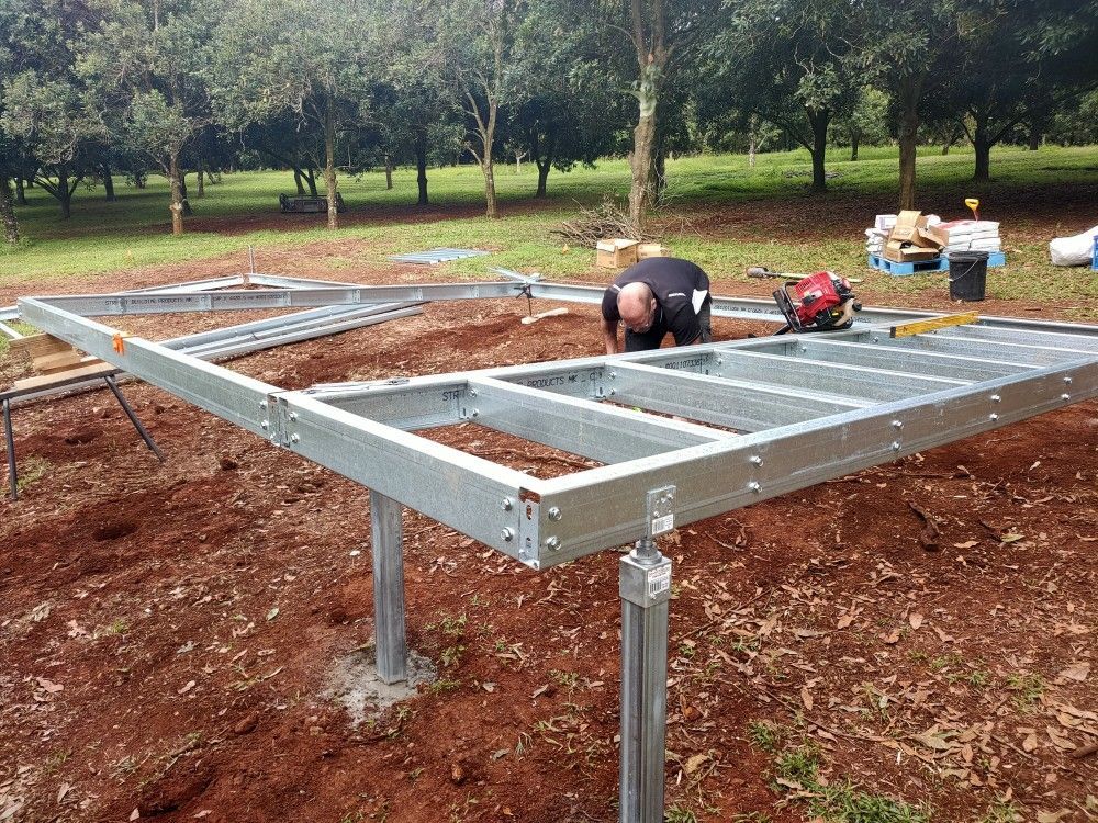 Metal frame structure under construction in a grassy outdoor area, with workers assembling it.