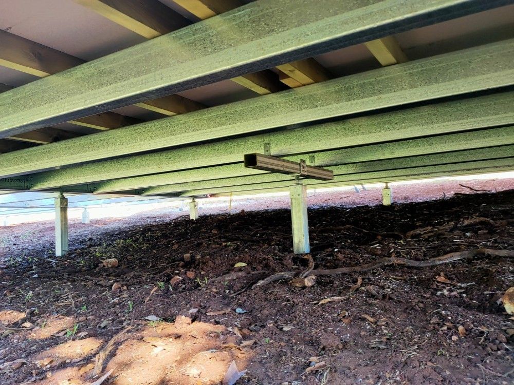 Underneath a raised green structure, showing support beams over dirt and debris