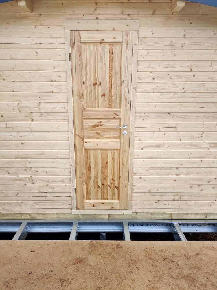 Wooden interior door set in a light pine-paneled wall, with a floor opening in front.