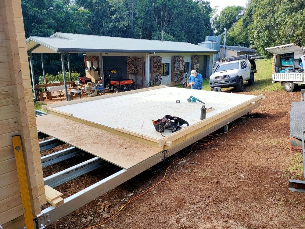 Partially built tiny house platform in a yard, with a worker and white van nearby