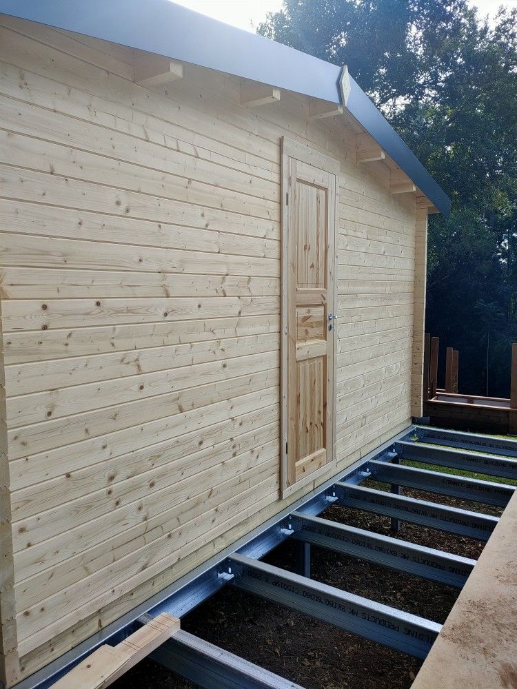 Wooden shed with light siding and a central door, viewed beside a metal-frame foundation under construction.