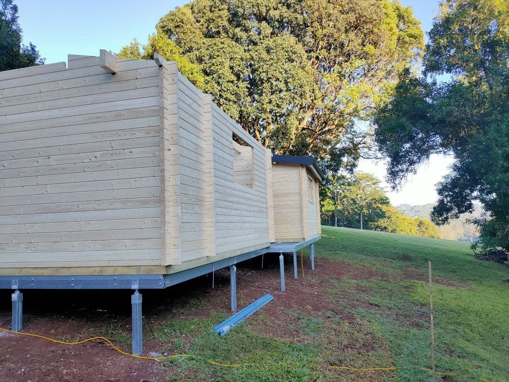 Wooden cabin on metal stilts beside a grassy hillside with trees in the background