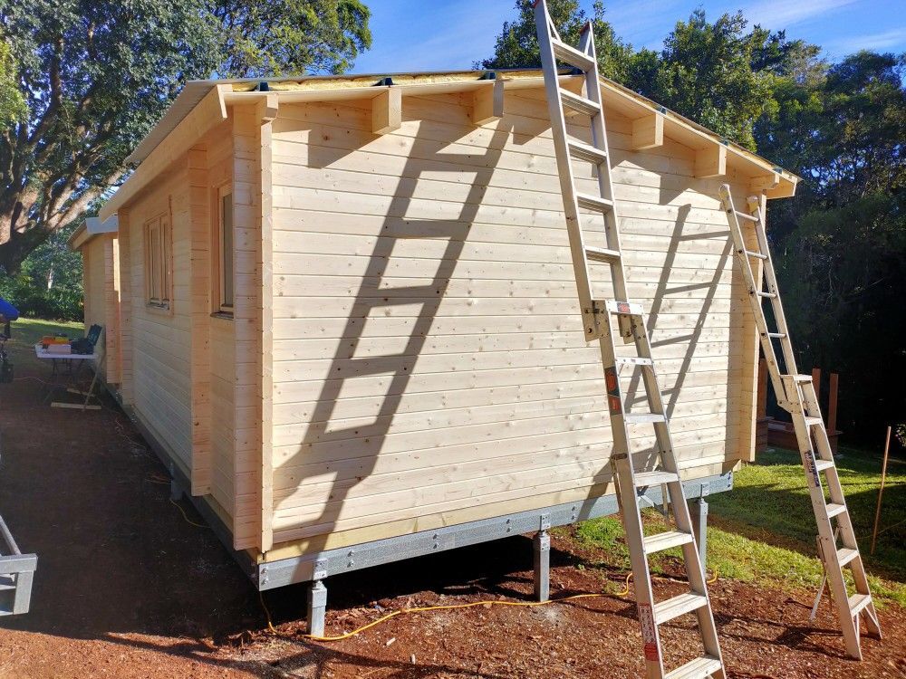 Wooden tiny house under construction with ladders leaning against it in a sunny yard
