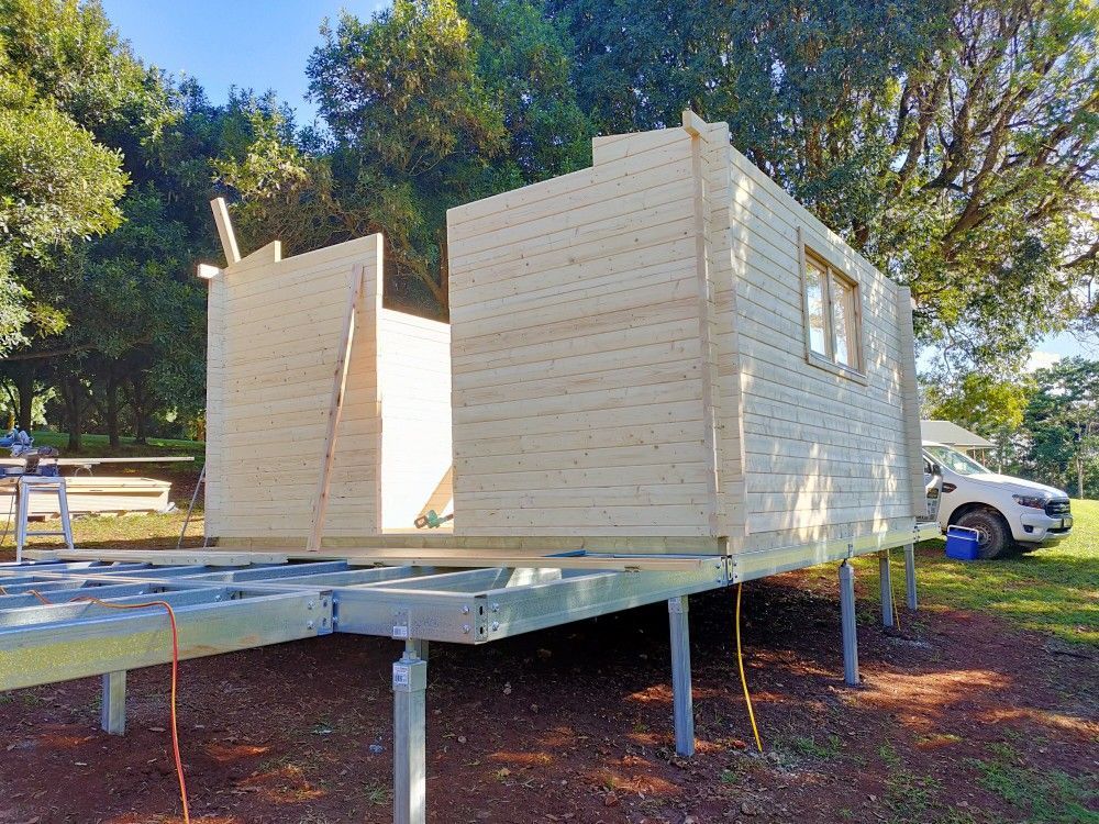 Elevated tiny house under construction on metal stilts, with pale wood siding and open doors outdoors.