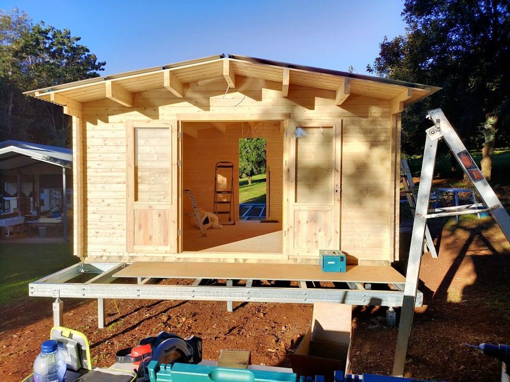 Small wooden shed under construction on a raised platform, with ladders and tools in a yard.