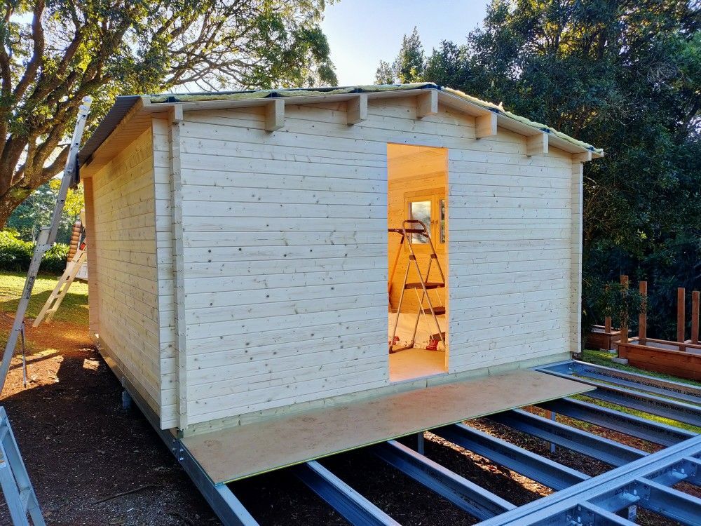 Small white house-like structure on metal rails, with an open doorway, outdoors among trees.