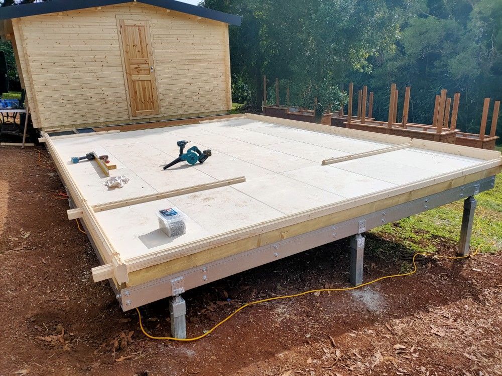 Raised house foundation under construction with white insulated panels, tools, and a small shed in the background
