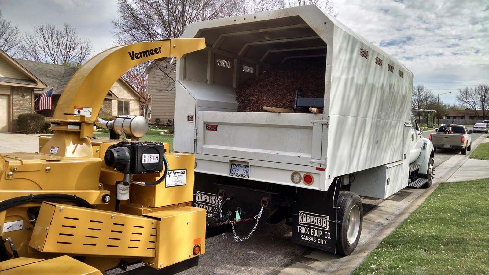A yellow machine is attached to the back of a white truck.