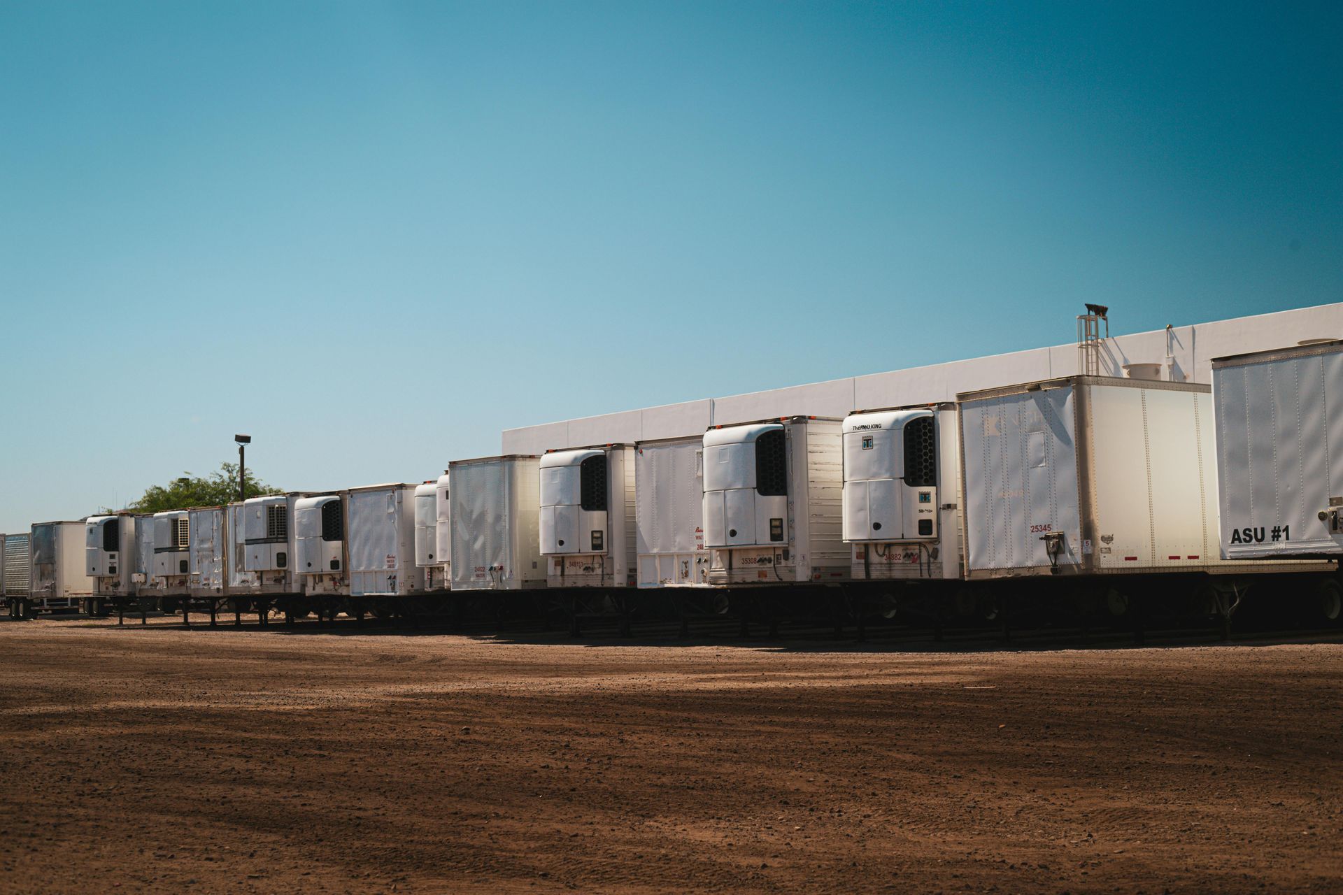 Refrigerated semi-truck trailers parked at a loading dock, against a clear blue sky.