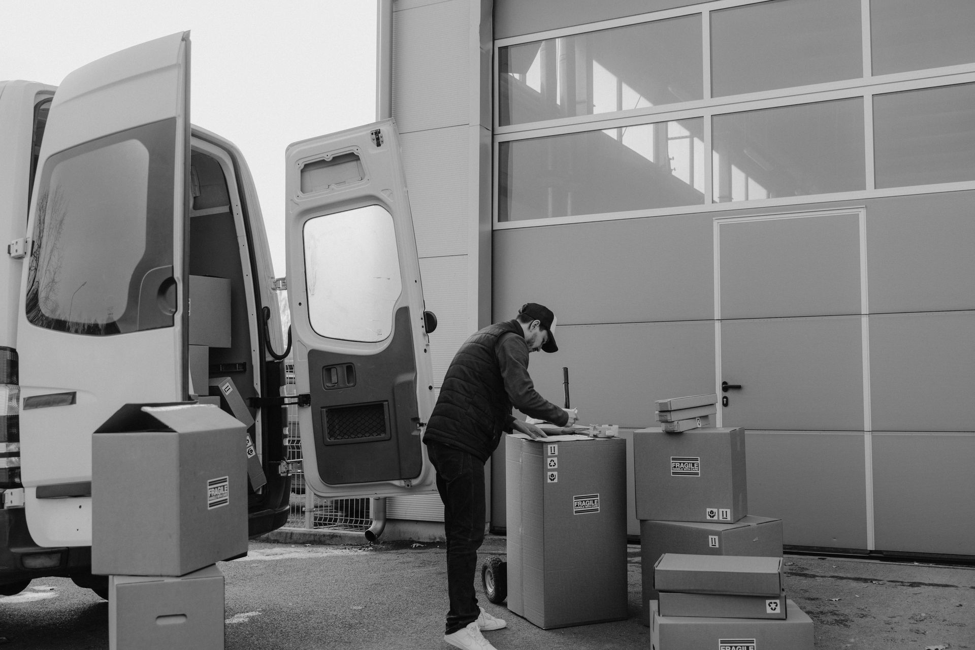 A person loads boxes into a cargo van parked near a warehouse door.