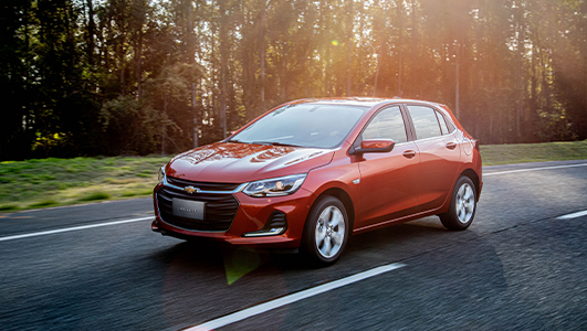 Um carro vermelho está dirigindo por uma estrada próxima a uma floresta.