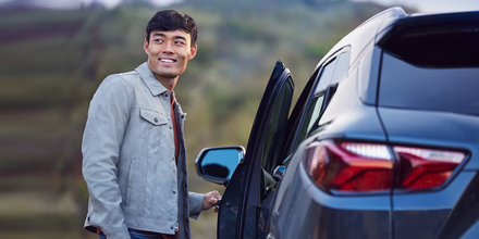 Um carro vermelho está dirigindo por uma estrada próxima a uma floresta.