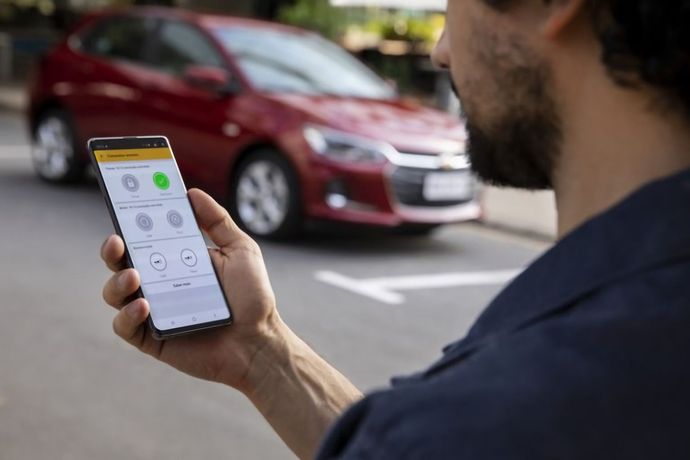 Um homem está segurando um telefone celular na frente de um carro vermelho.