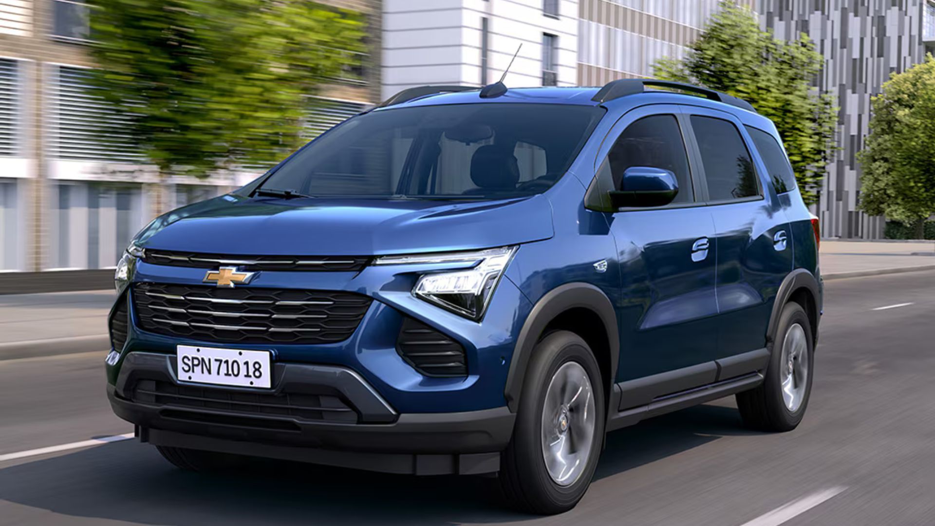 Blue Chevrolet SUV driving on a city street near modern buildings
