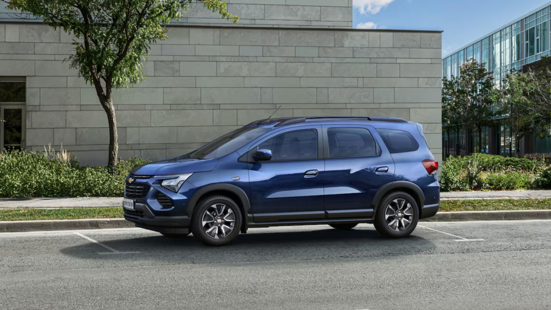 Blue SUV parked on a street beside a stone wall and greenery.