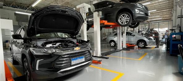 Two cars on lifts in an auto repair shop, with one black car’s hood open in the foreground.