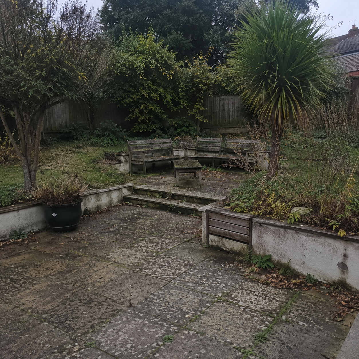 Small overgrown garden patio with stone benches, steps, and a paved seating area