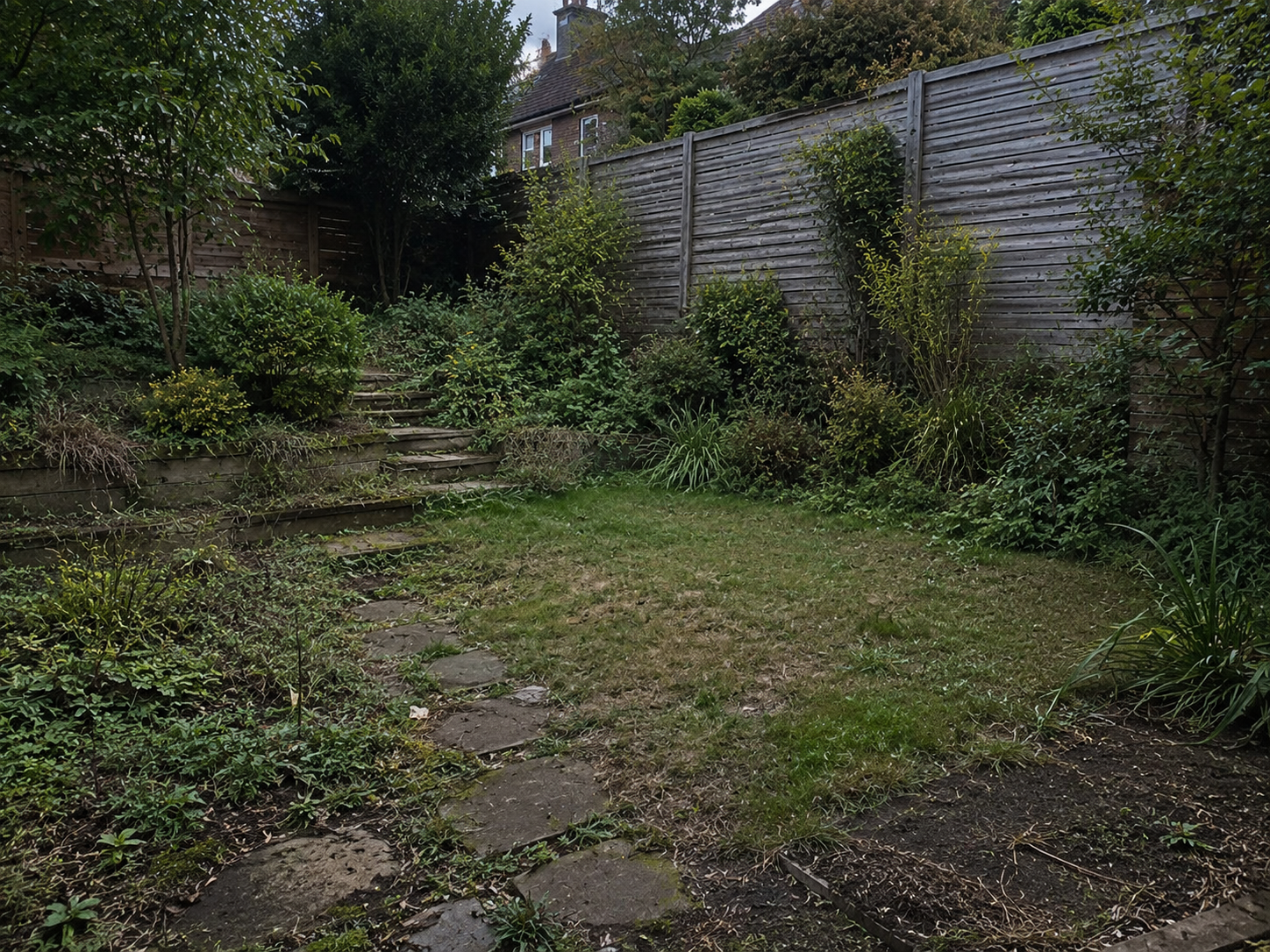 Backyard garden with stone steps, grassy lawn, shrubs, and a tall wooden fence