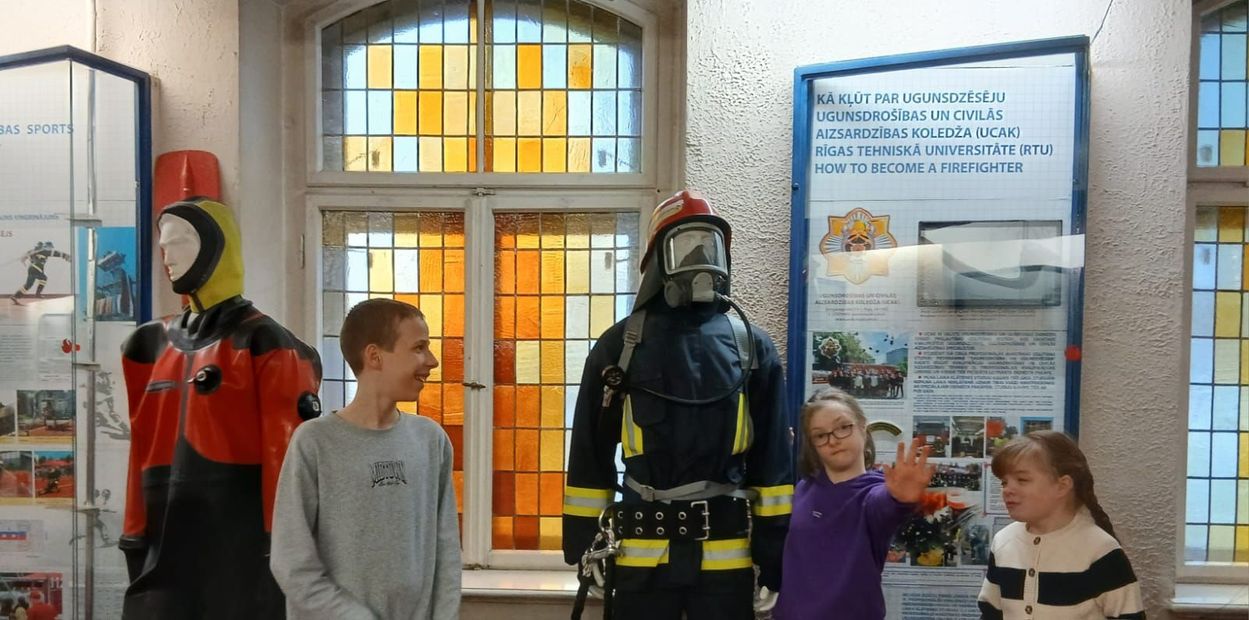 Two children stand near two mannequins dressed in professional safety gear inside a room with stained-glass windows.