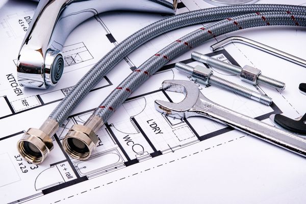 Tools, tubing, and a tape measure on blueprints for a plumbing installation plan