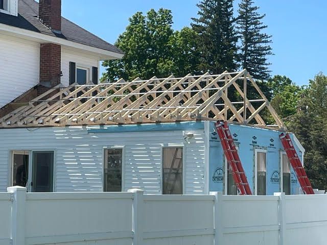 Construction site: new roof being built on a white building, wood frame exposed, blue wrap, red ladders.
