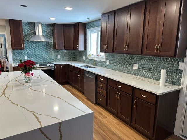 A renovated kitchen with dark brown cabinets, a white countertop, and turquoise backsplash.