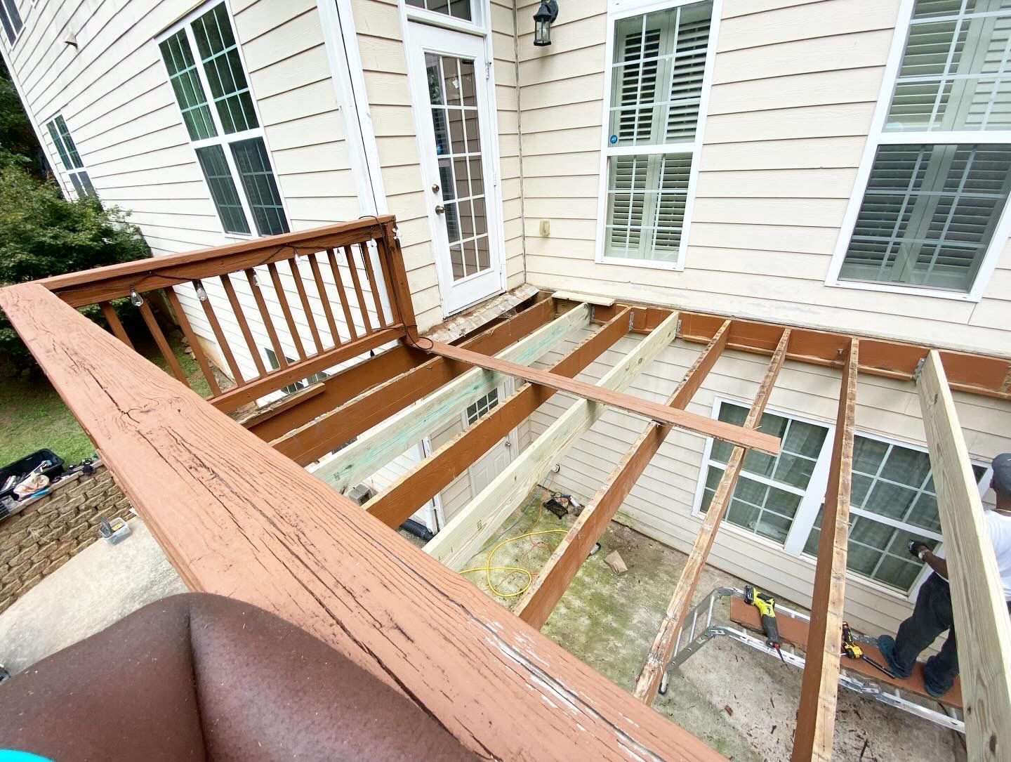 Deck construction in progress; wooden frame, partially built, attached to a house with a door and windows.