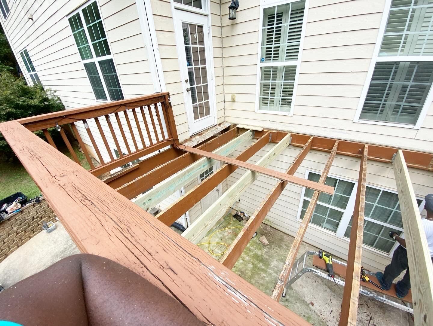 Deck construction in progress; wooden frame with existing railing next to a house with windows.
