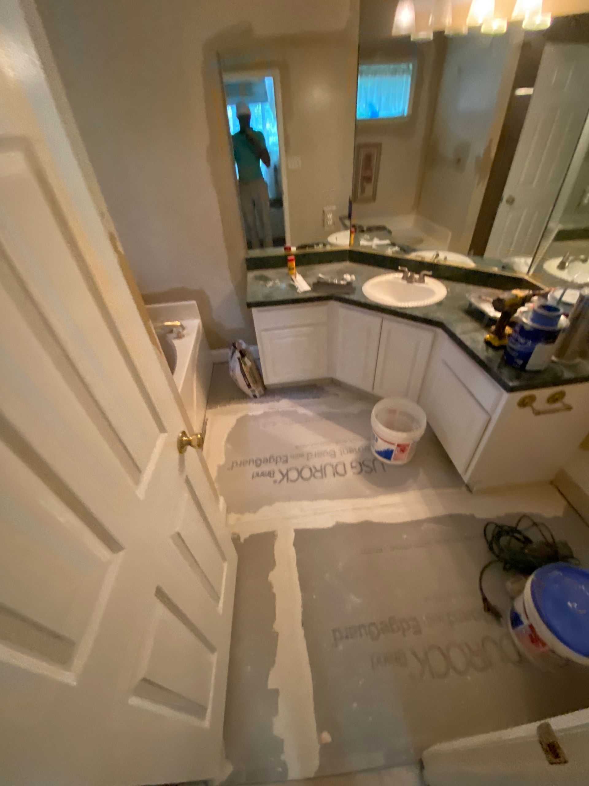 Bathroom under renovation, with white cabinets, green countertop, and doorway with person visible.