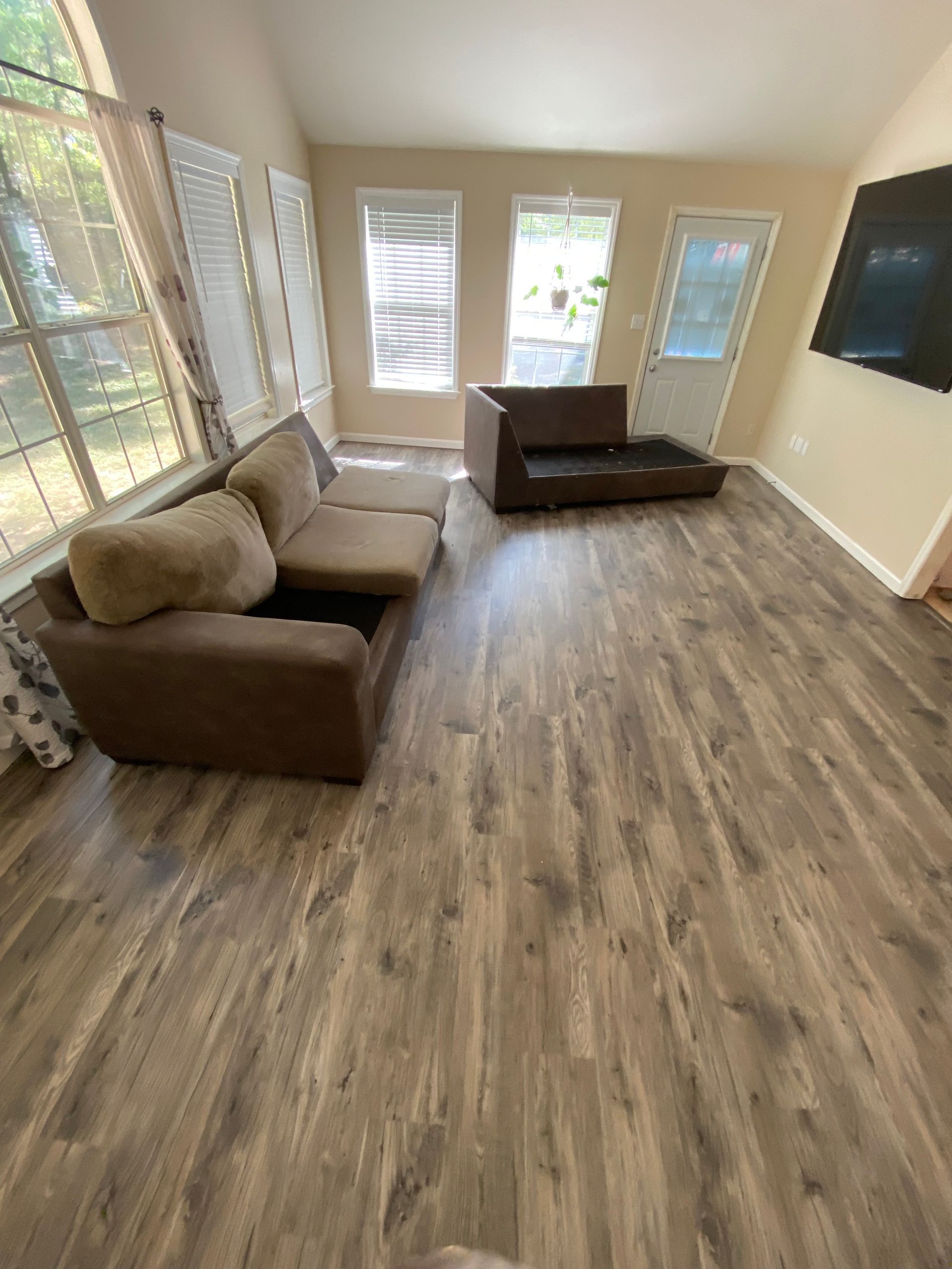 Living room with brown sectional sofa, wooden floor, windows, and a TV.