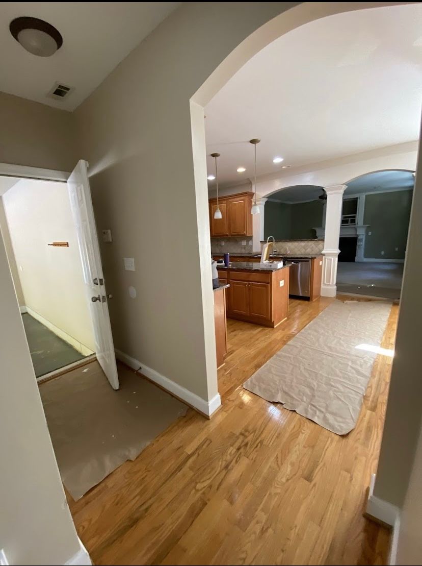Hallway leads to kitchen, entryway to a utility room on the left. Hardwood floors, tan walls.