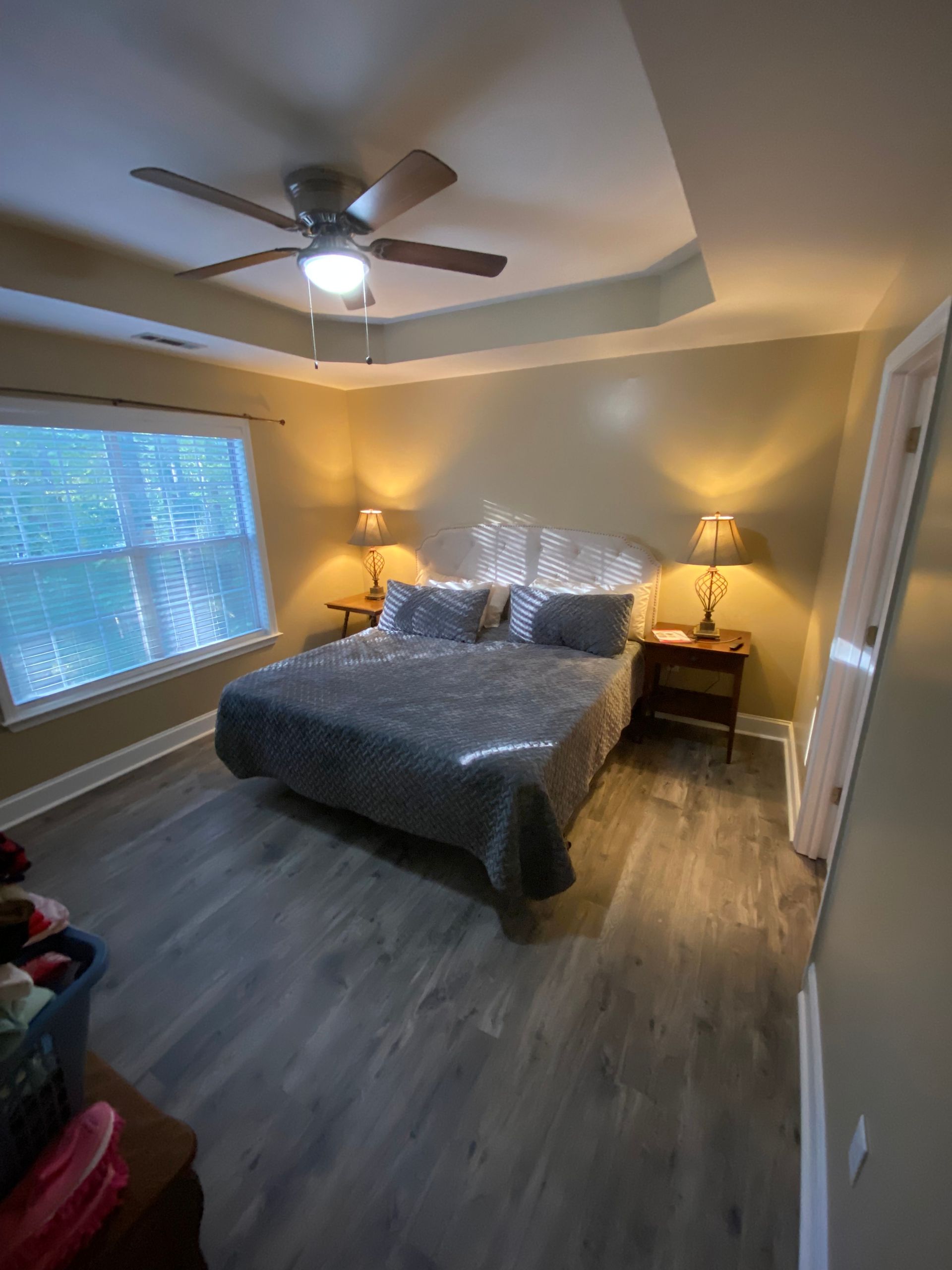 Bedroom with bed, nightstands, lamps, and ceiling fan; neutral tones, natural light.