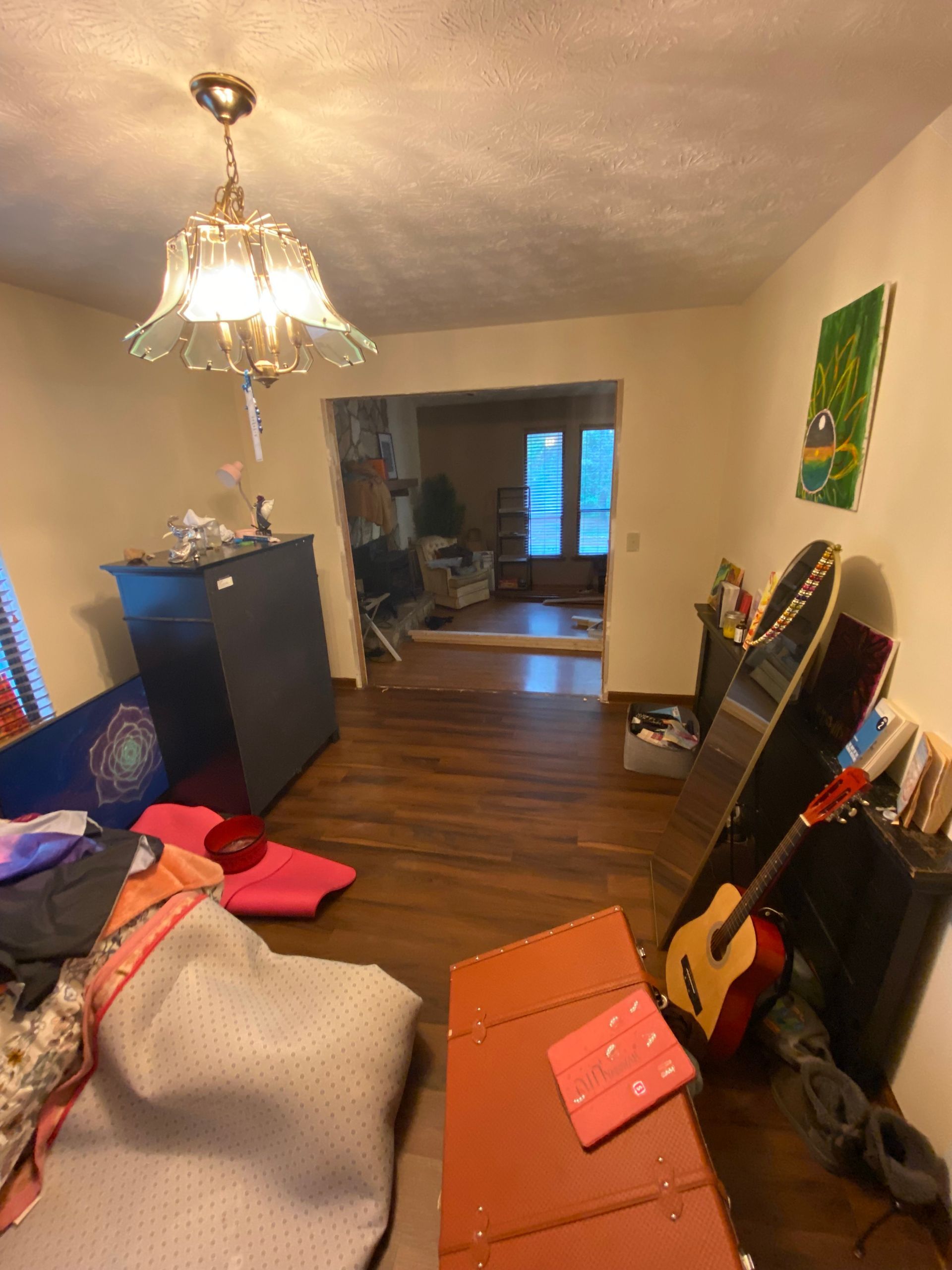 Room with cluttered furniture, open doorway to another room with a window, dark wood floors.