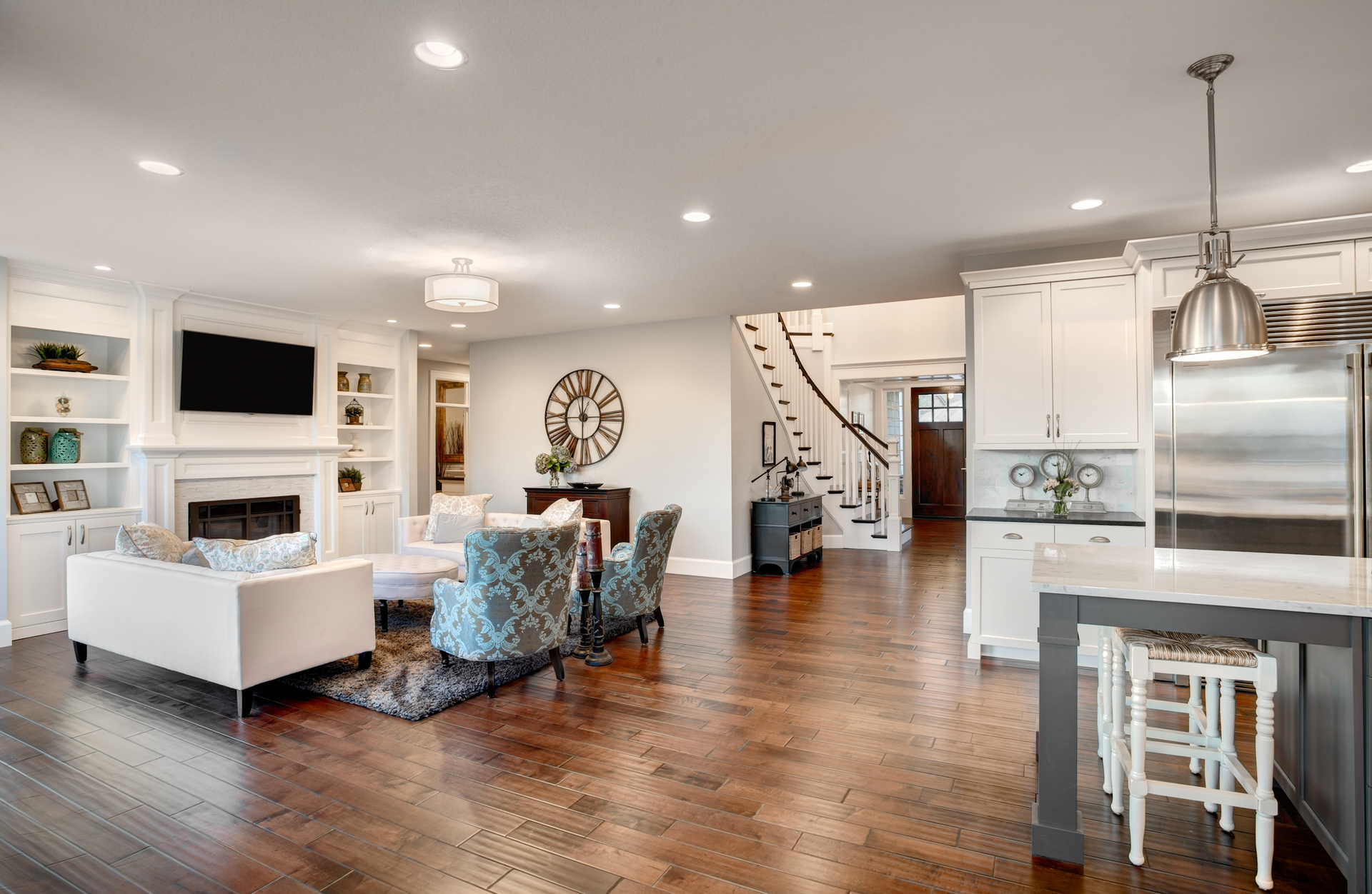 Spacious living room with fireplace, white furniture, and kitchen with island and stainless steel appliances.