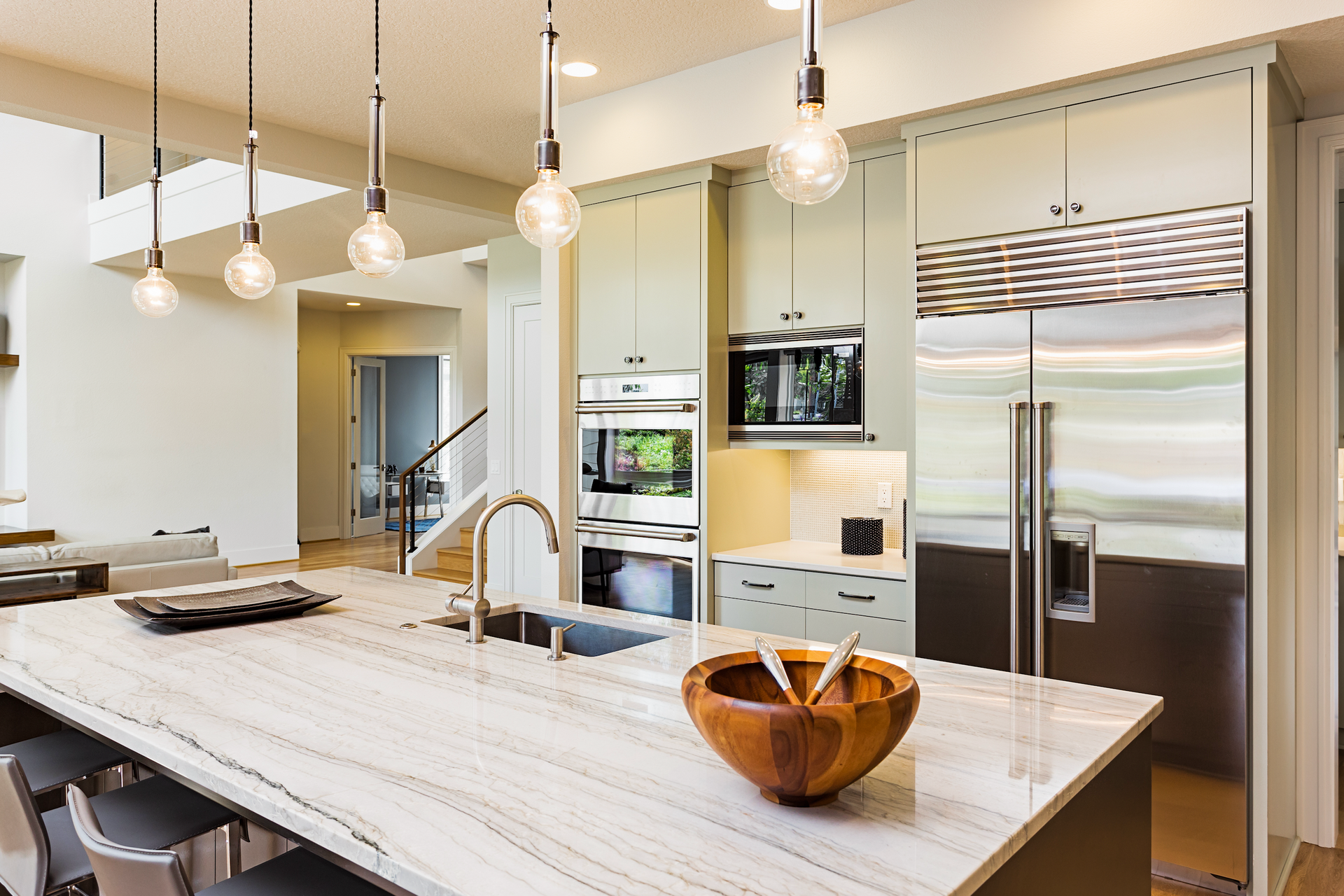 Modern kitchen with island, stainless steel appliances, light wood cabinets, and pendant lights.