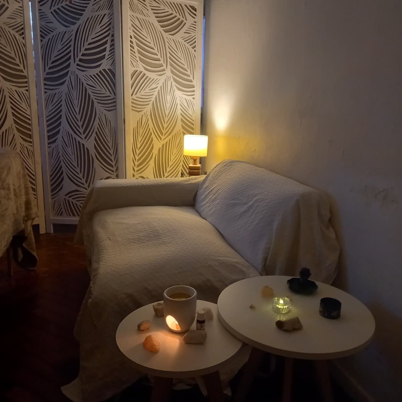 Acogedora sala de estar con un sofá blanco, lámparas encendidas y mesitas redondas con tazas y velas.