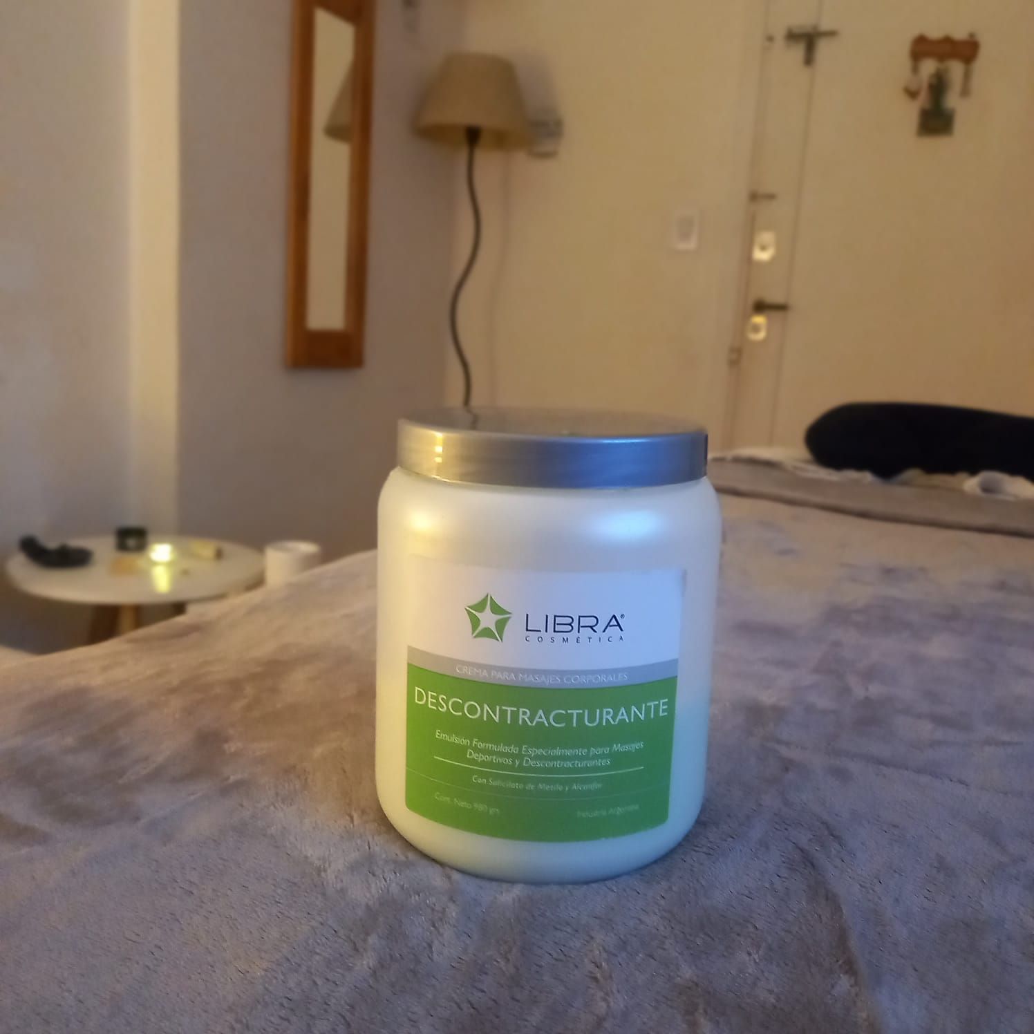 Tarro blanco de crema para la piel con etiqueta verde sobre una cama, en un dormitorio