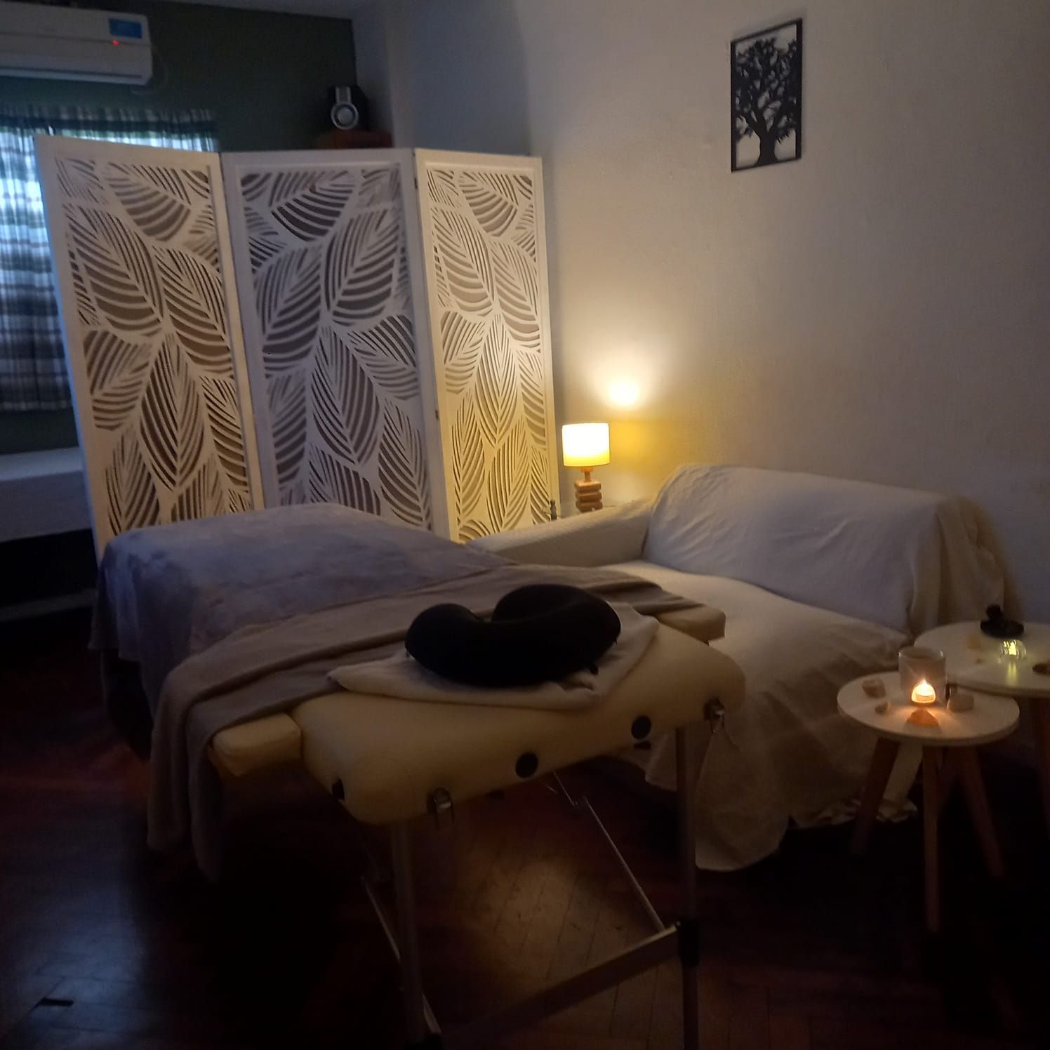 Sala de masajes tenue, con dos camillas, una lámpara encendida y un biombo decorativo.