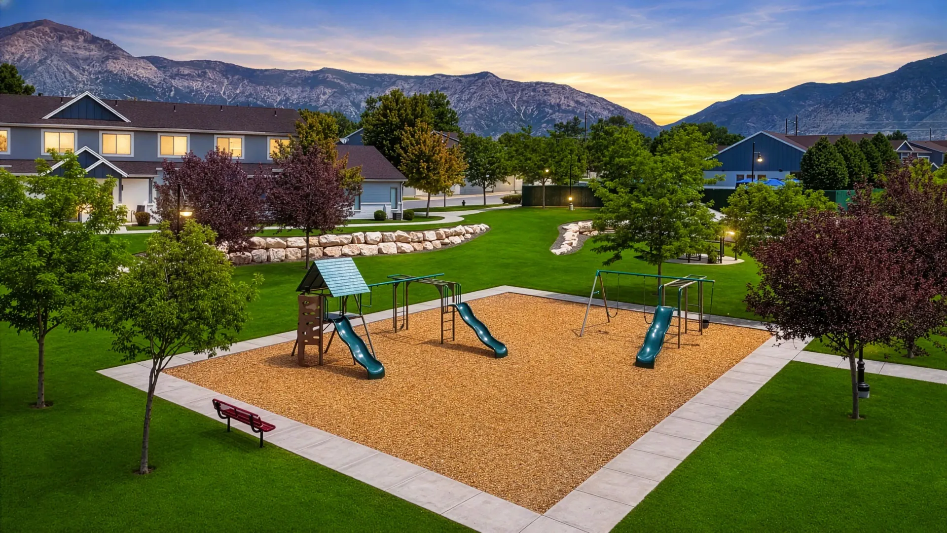 Playground with swings, slides, and jungle gym, surrounded by manicured lawns and trees, with apartment buildings and mountains in the background at Mountain View Townhomes, offering townhomes in Ogden, UT.