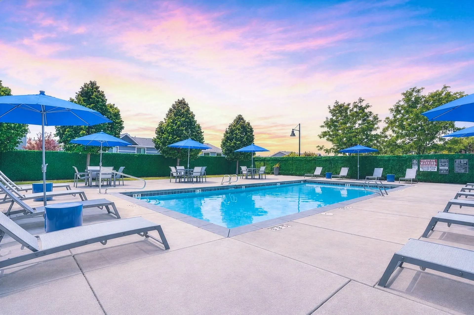 Outdoor swimming pool with lounge chairs and umbrellas under a colorful sky at Mountain View Townhomes, offering townhomes in Ogden, UT.