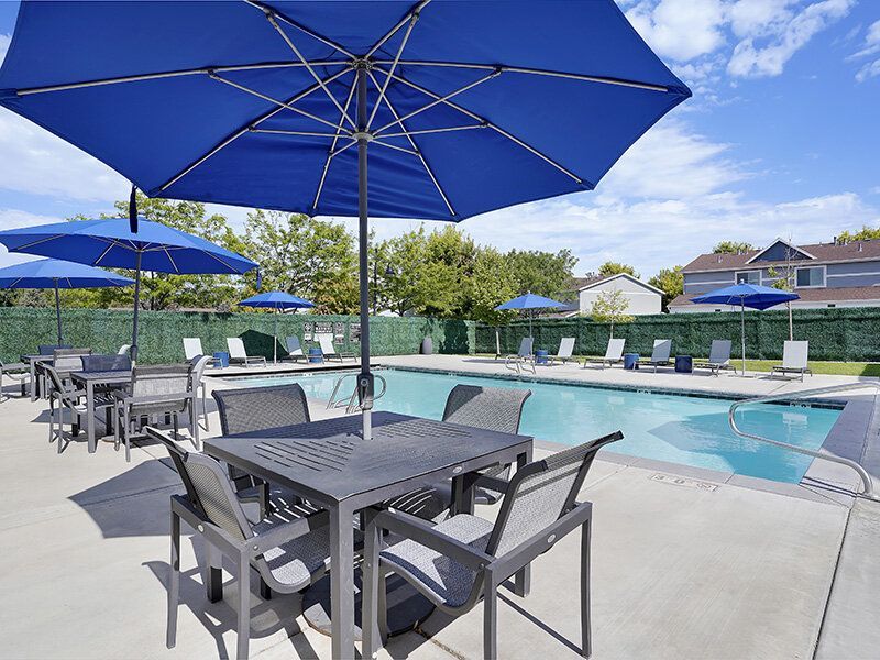 Mountain View Townhomes apartment pool area with blue tables, chairs, and umbrellas.