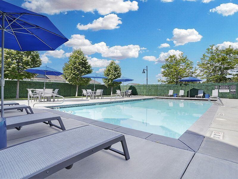 Mountain View Townhomes pool area with lounge chairs, blue umbrellas, and a clear blue sky.