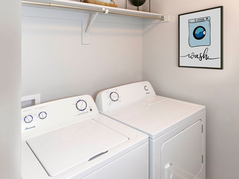 Mountain View Townhomes  laundry room with two white top-loading washers and a matching dryer, plus a framed 'wash' art print.