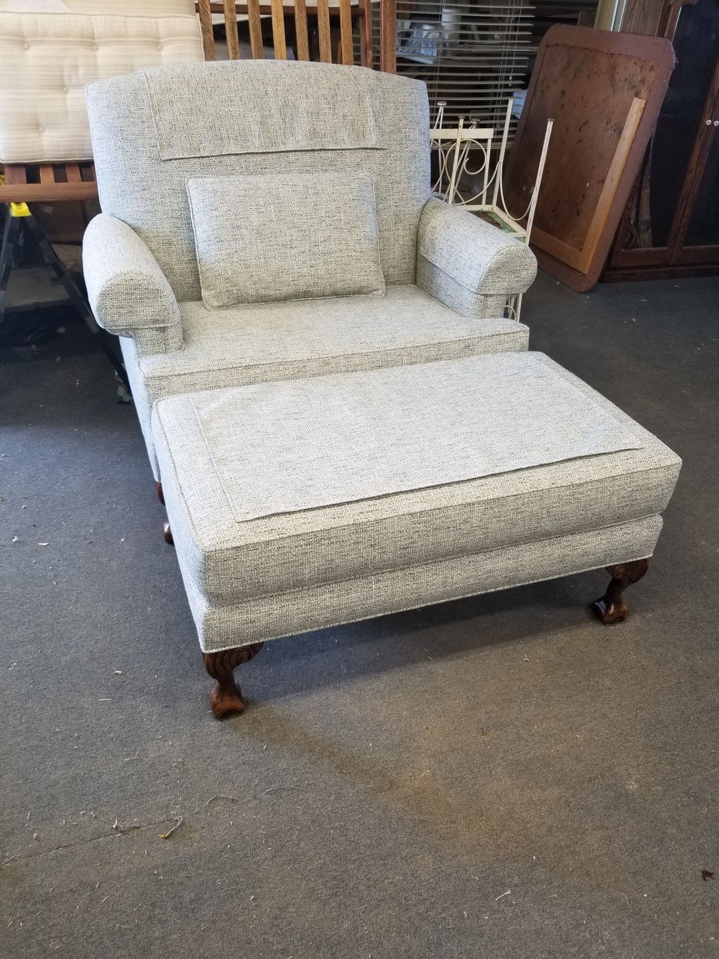 Upholstered armchair and ottoman with light gray speckled fabric and dark wood feet, indoors.
