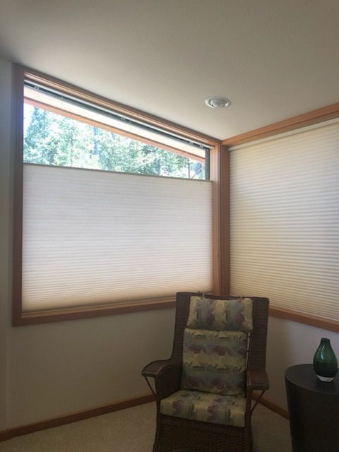 Corner room with two windows, one angled, with light beige cellular shades. A chair sits below the angled window.