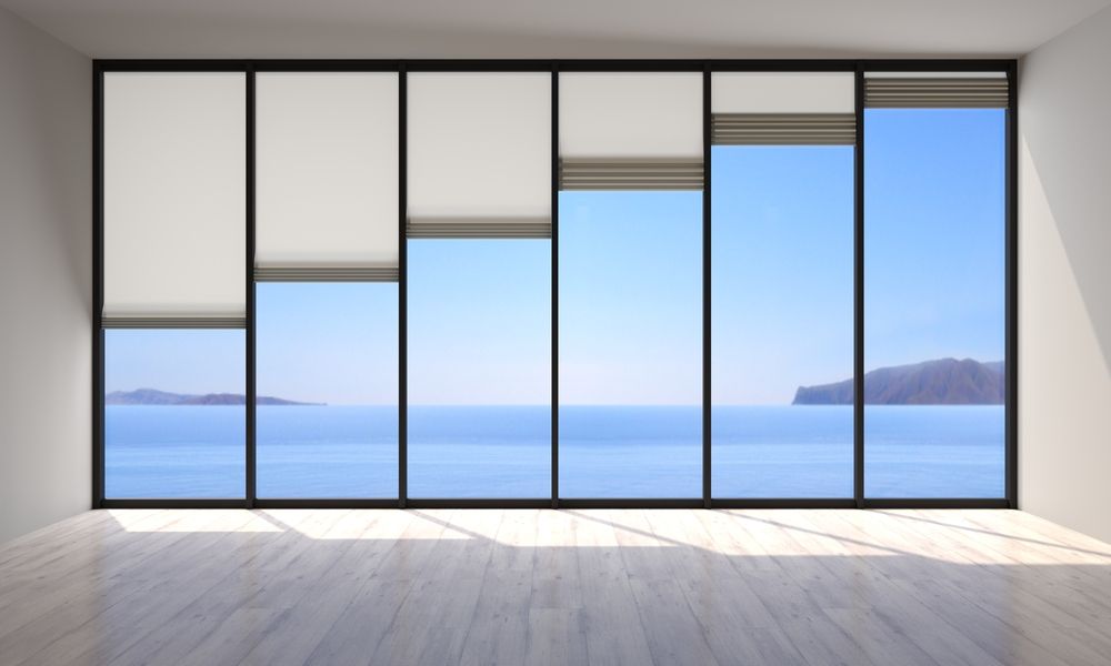 Large window with partially lowered blinds; ocean and sky view.