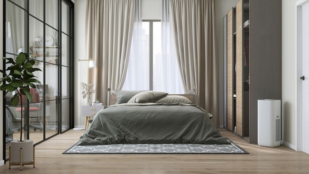 A bedroom with a bed, large window with curtains, and wardrobe. A green rug and a potted plant are visible.
