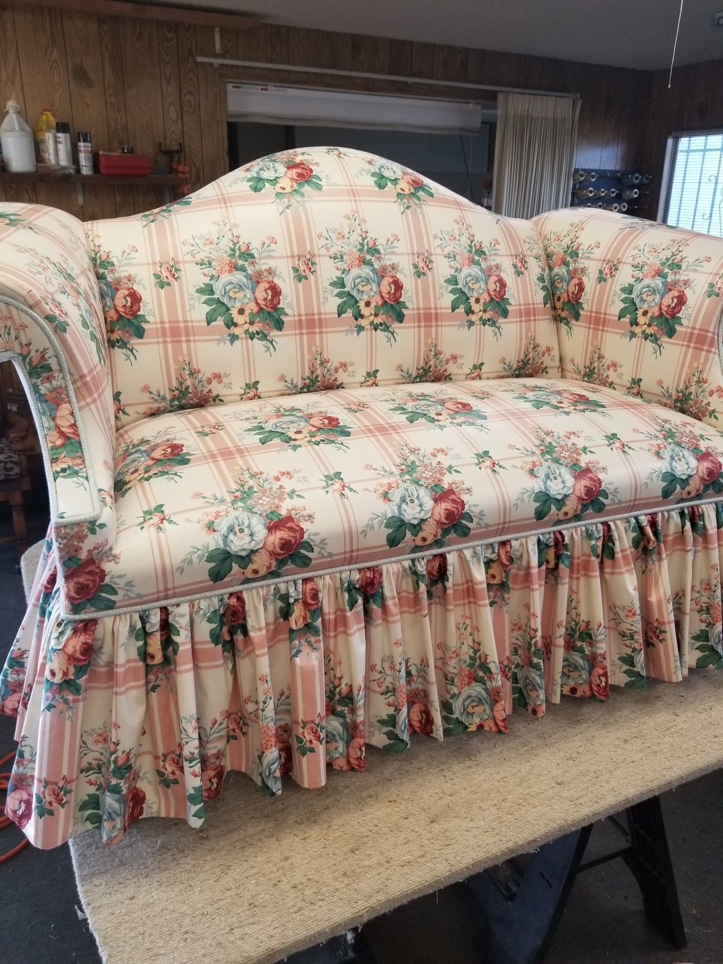 Floral patterned loveseat with ruffled skirt sits on a workbench.